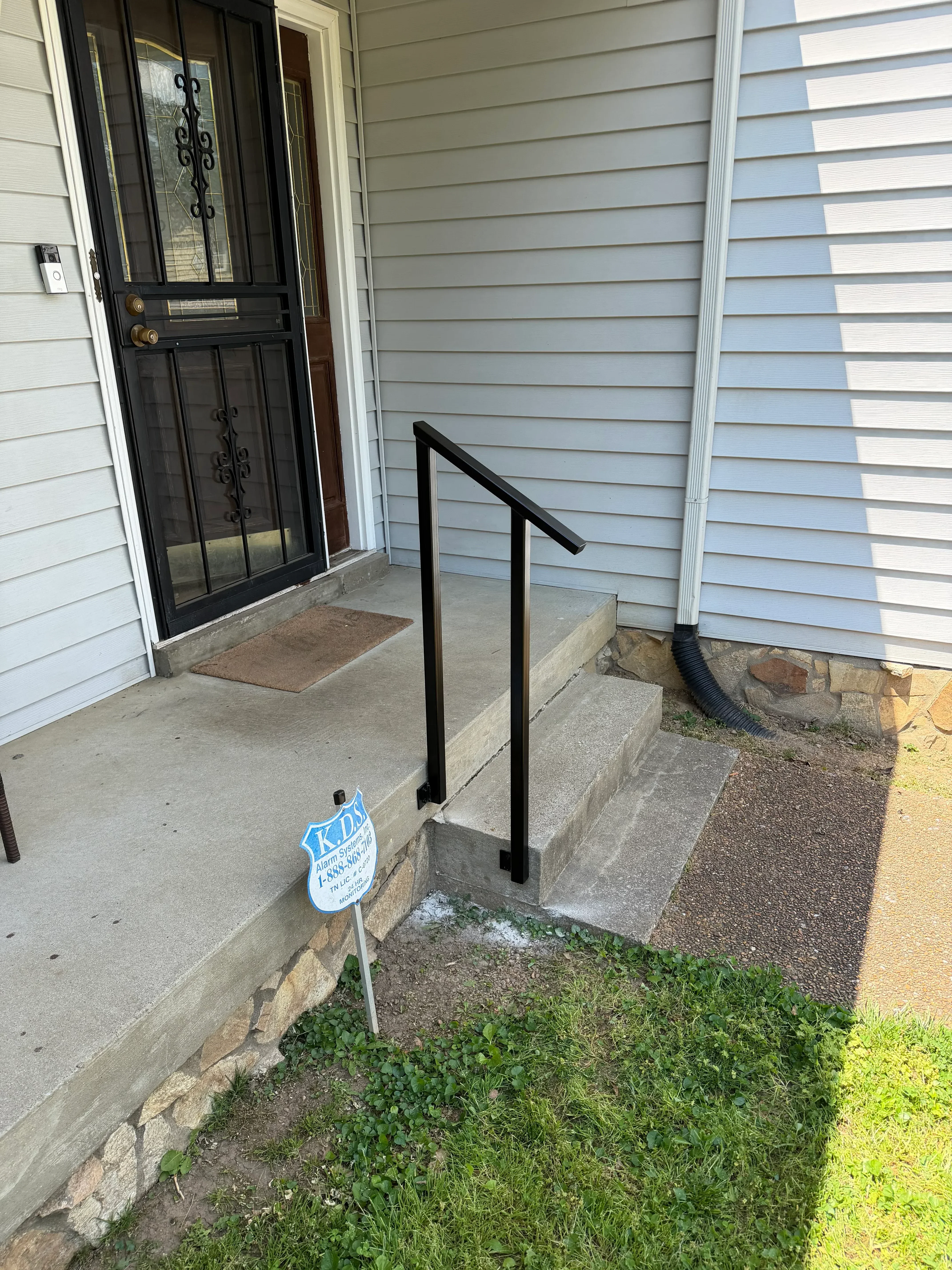 Black metal handrails installed on concrete steps at residential entry with corrugated siding