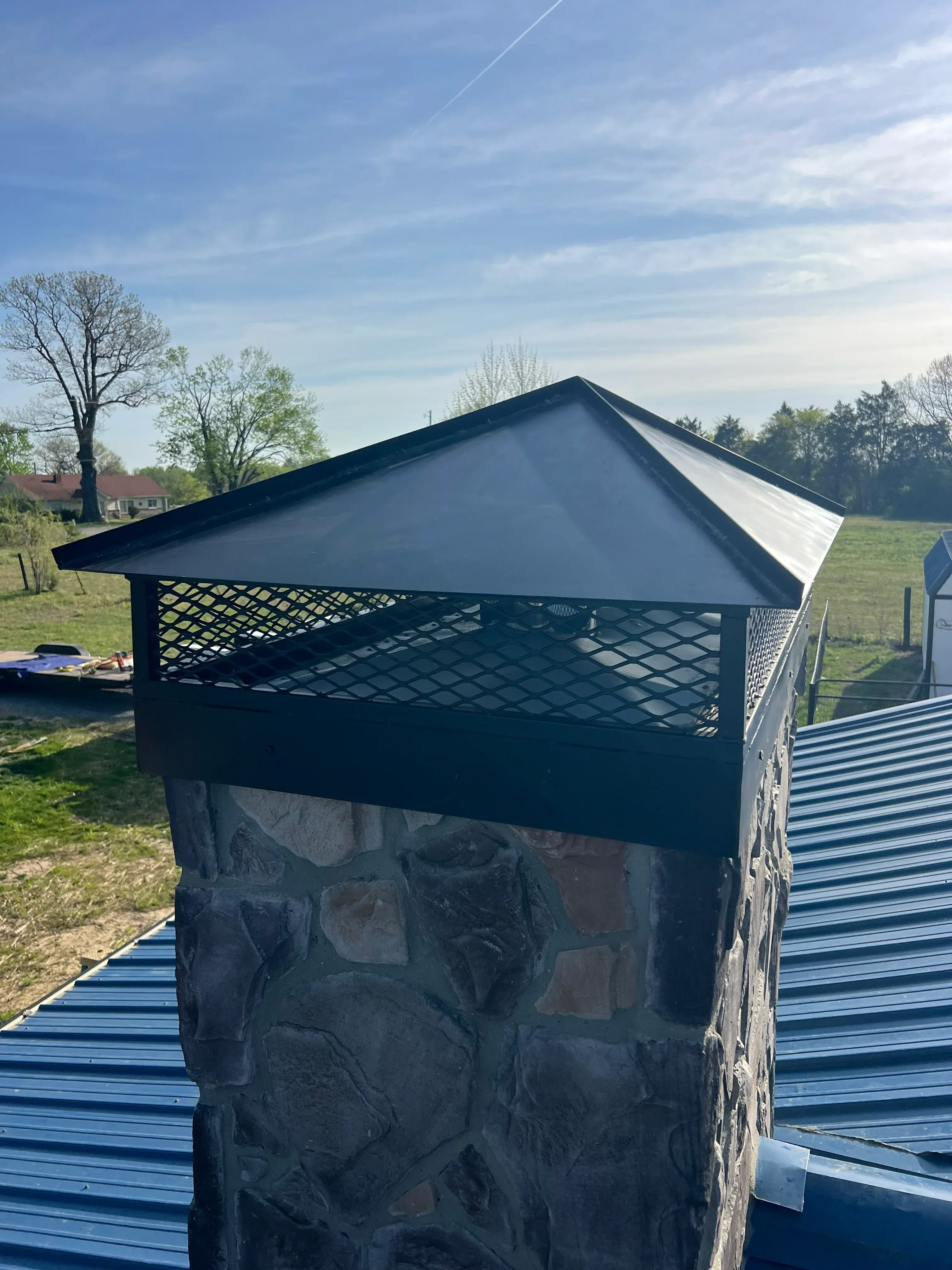 Welded steel enclosure with diamond plate mesh panels and sloped metal roof on stone base