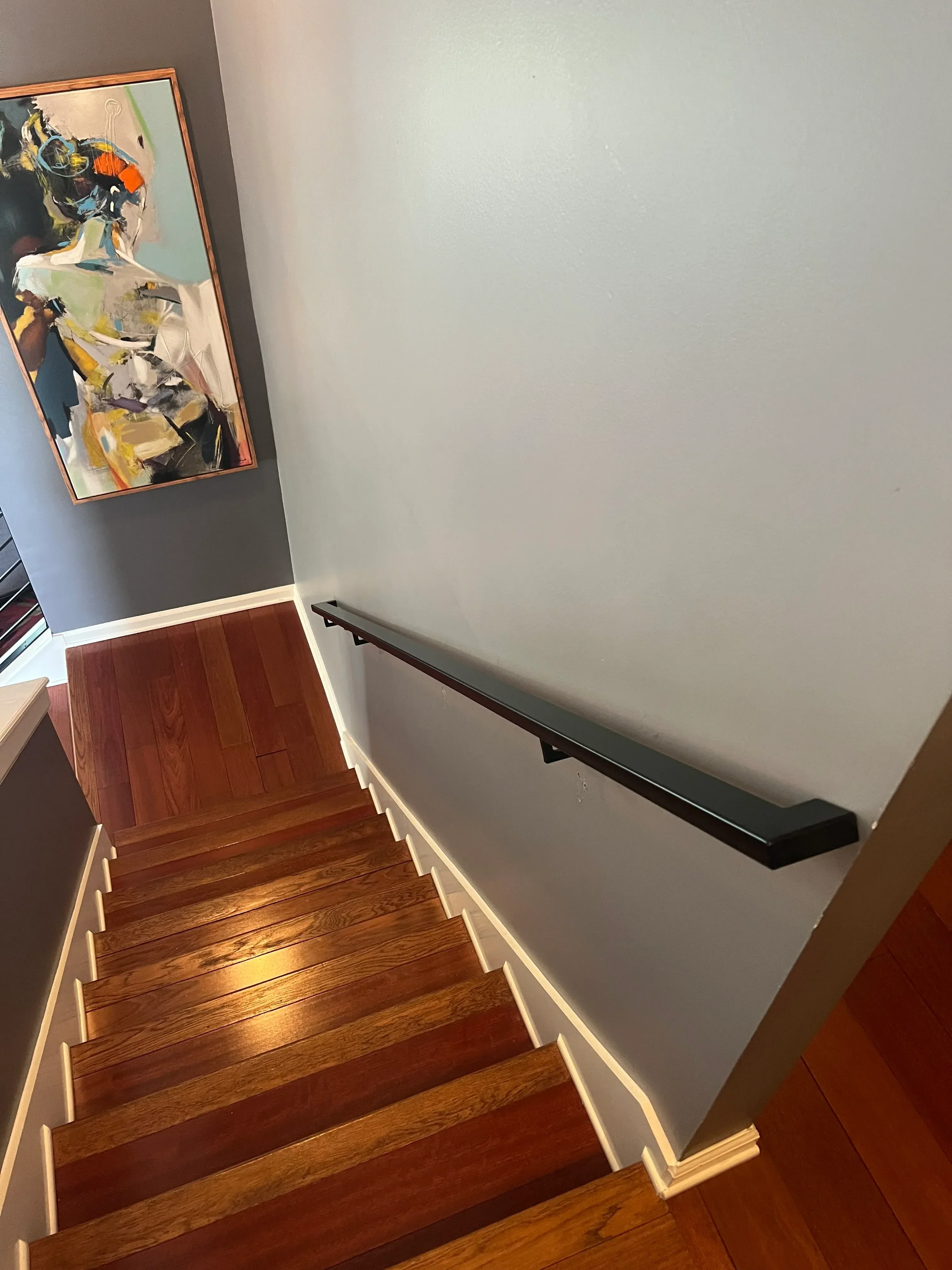 Black metal handrail with LED lighting on wooden staircase with white drywall