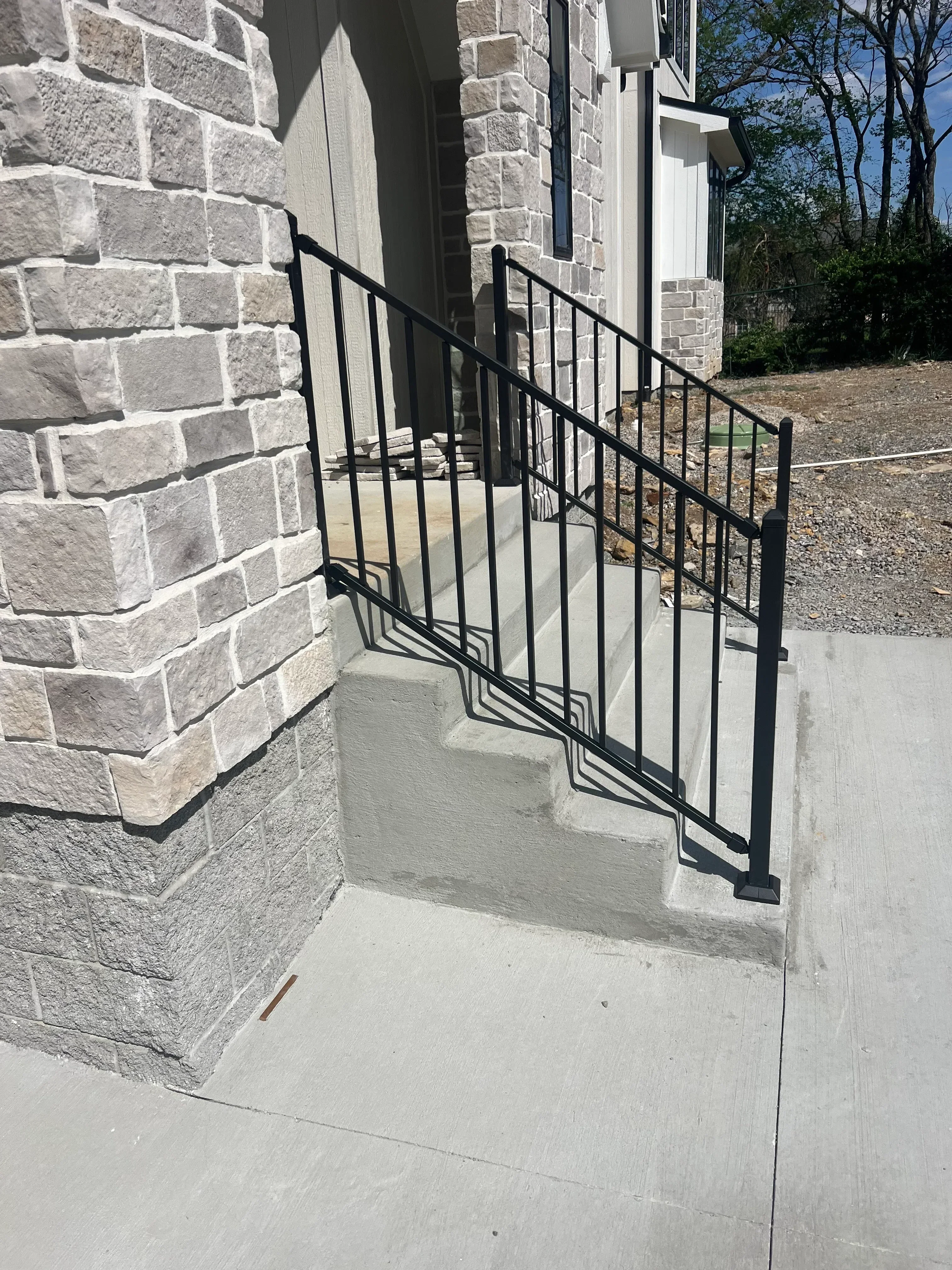 Black metal stair railing with horizontal bars on stone steps and concrete wall