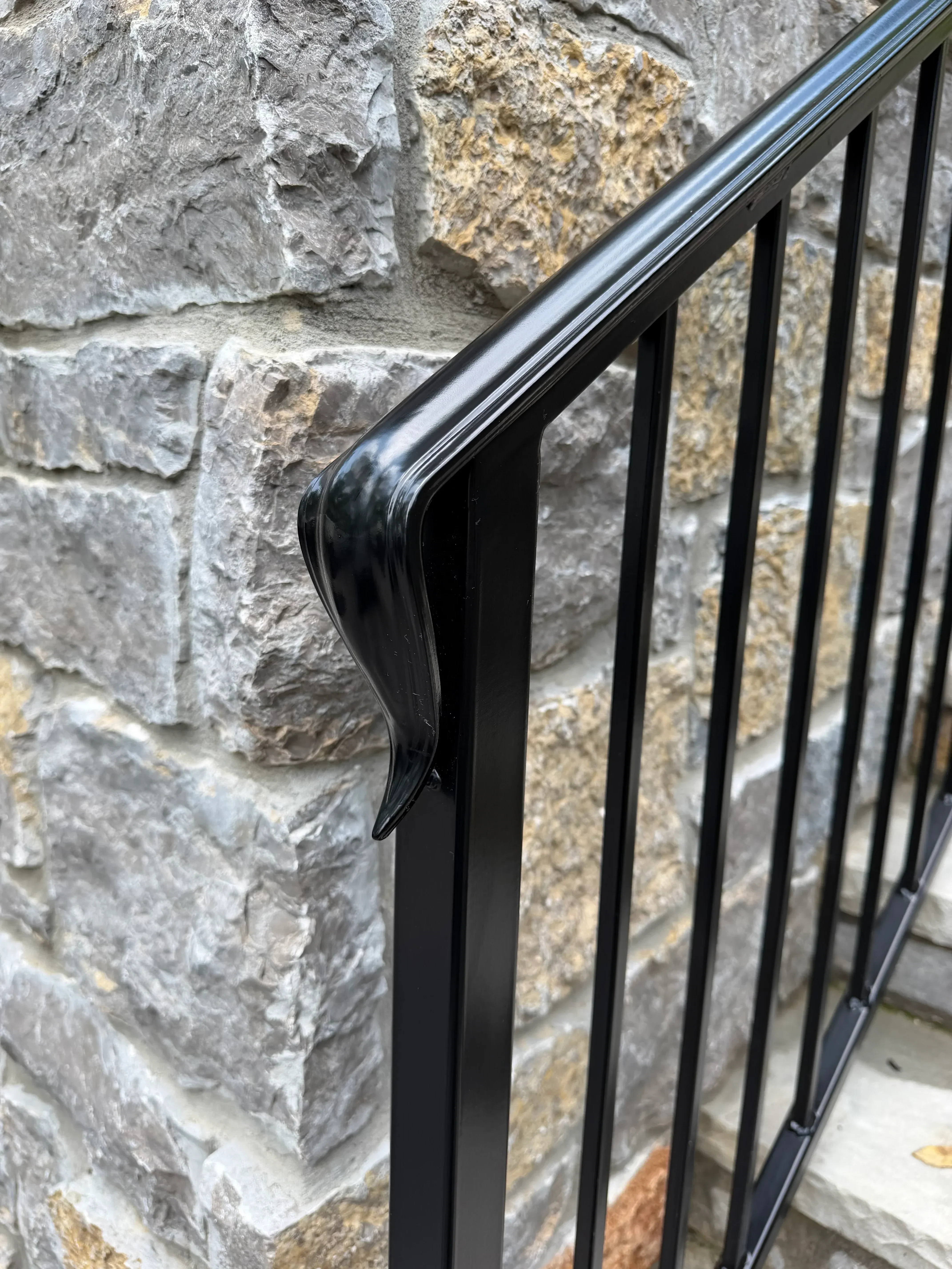 Black metal railing with horizontal slats and curved handrail on stone wall