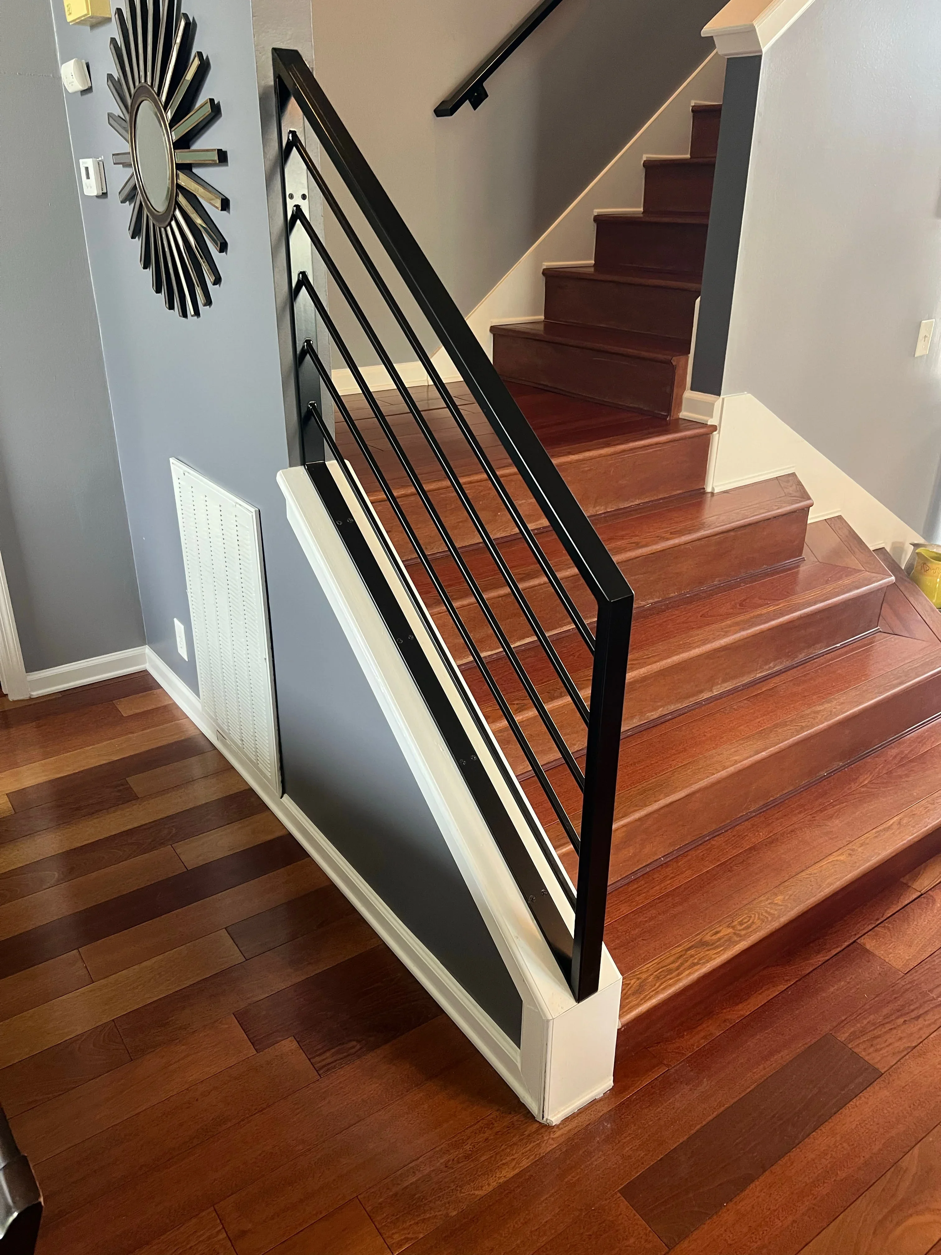 Black metal stair railing with horizontal cable balusters and white trim on hardwood stairs