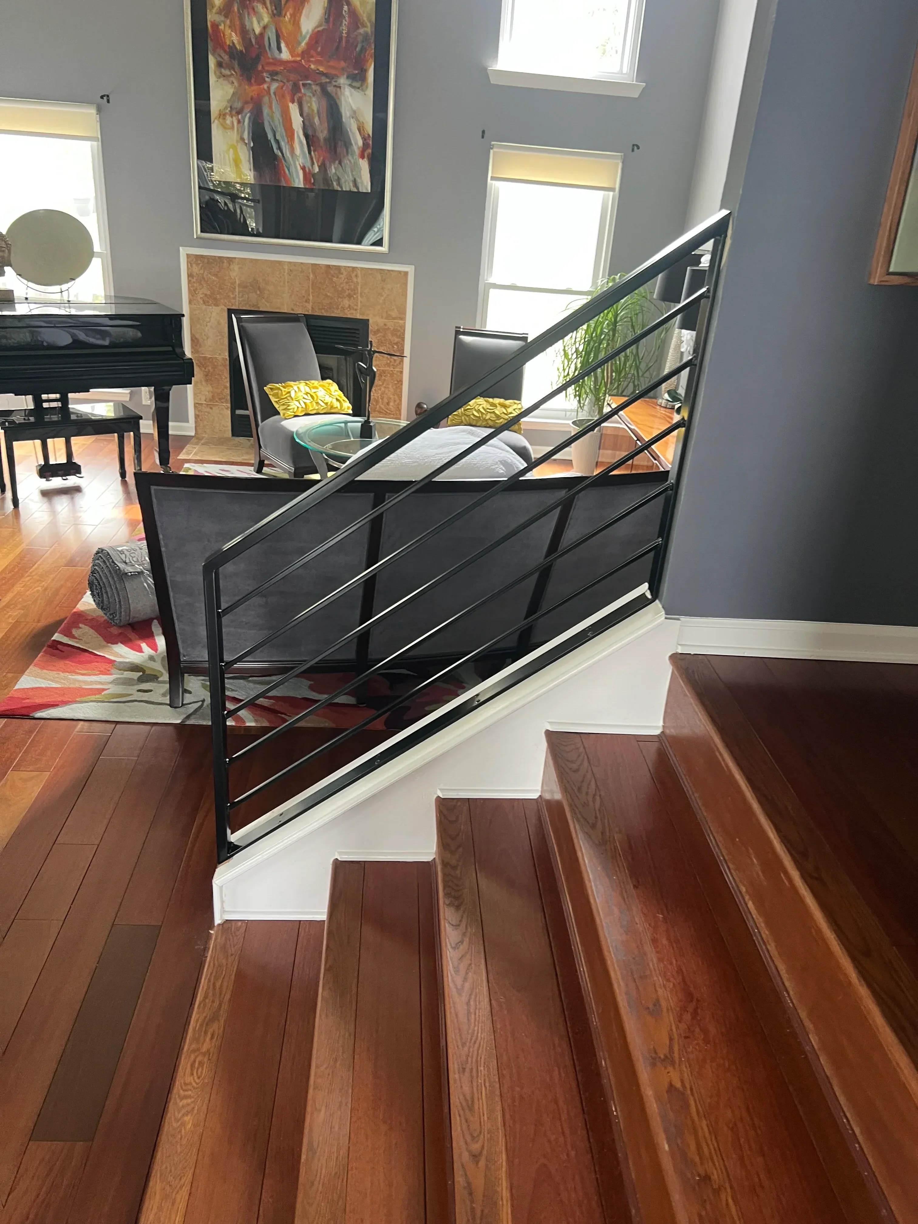 Black metal stair railing with diagonal bracing and glass panels on wooden stairs