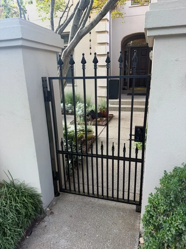A custom metal gate at the driveway entrance of a residential property in Nashville, Tennessee, with metal fencing extending along the property line. The fabricated metalwork shows clean welds and a finished surface suited for Middle Tennessee's outdoor conditions.